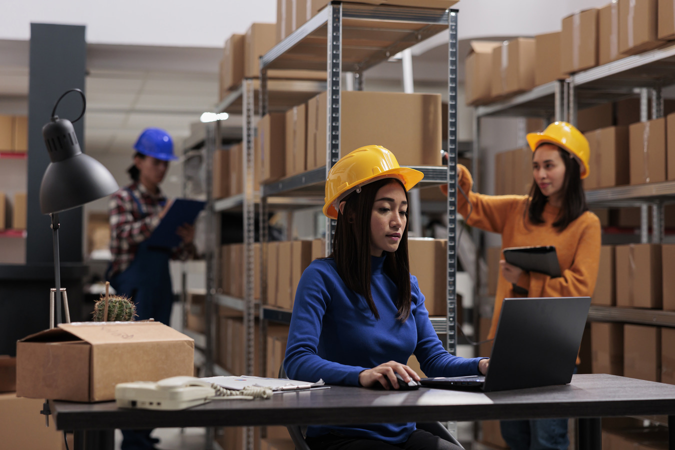 Women in yellow hardhat working on laptop in warehouse